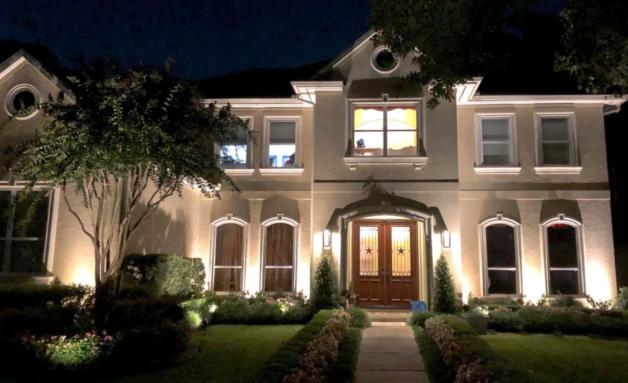 A large 2 story home with a free in front is lit up by Houston residential lighting