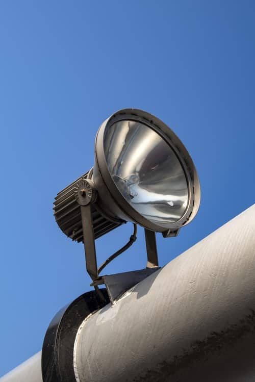 Outdoor LED lighting fixture perched on the top of a thick horizontal pole against blue sky