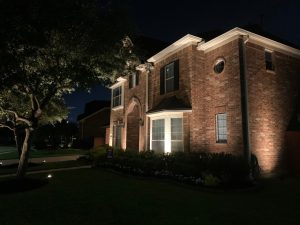 A brick house lit up at night with uplighting, one of the many different types of landscape lighting