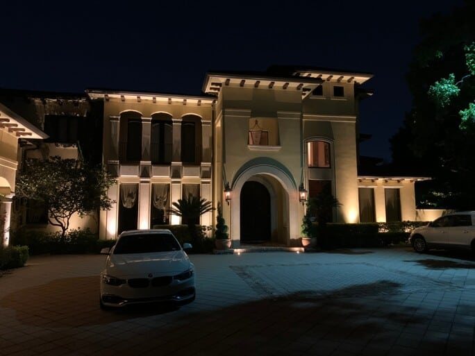 The memorial villages tx villa lit up at night with 2 cars on the left and right side of the driveway