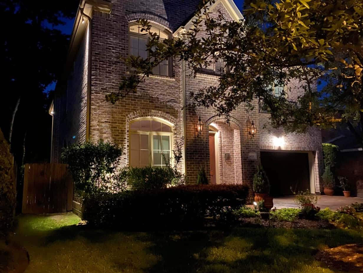 A brick house at night with a tree in front illuminated by fall landscape lighting