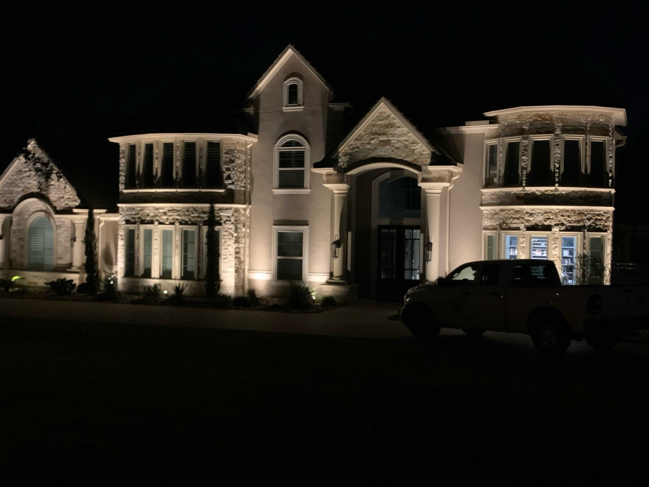 The front of the Woodlands Houston Home lit up at night with a truck parked in front