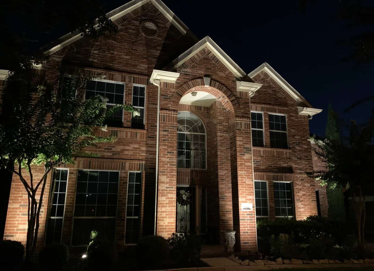 Uplighting on a 2 story brick house at night with a tree in front