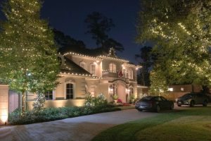 A 2 story house decorated with winter lights for Christmas, with two trees in the front and 2 cars in the driveway