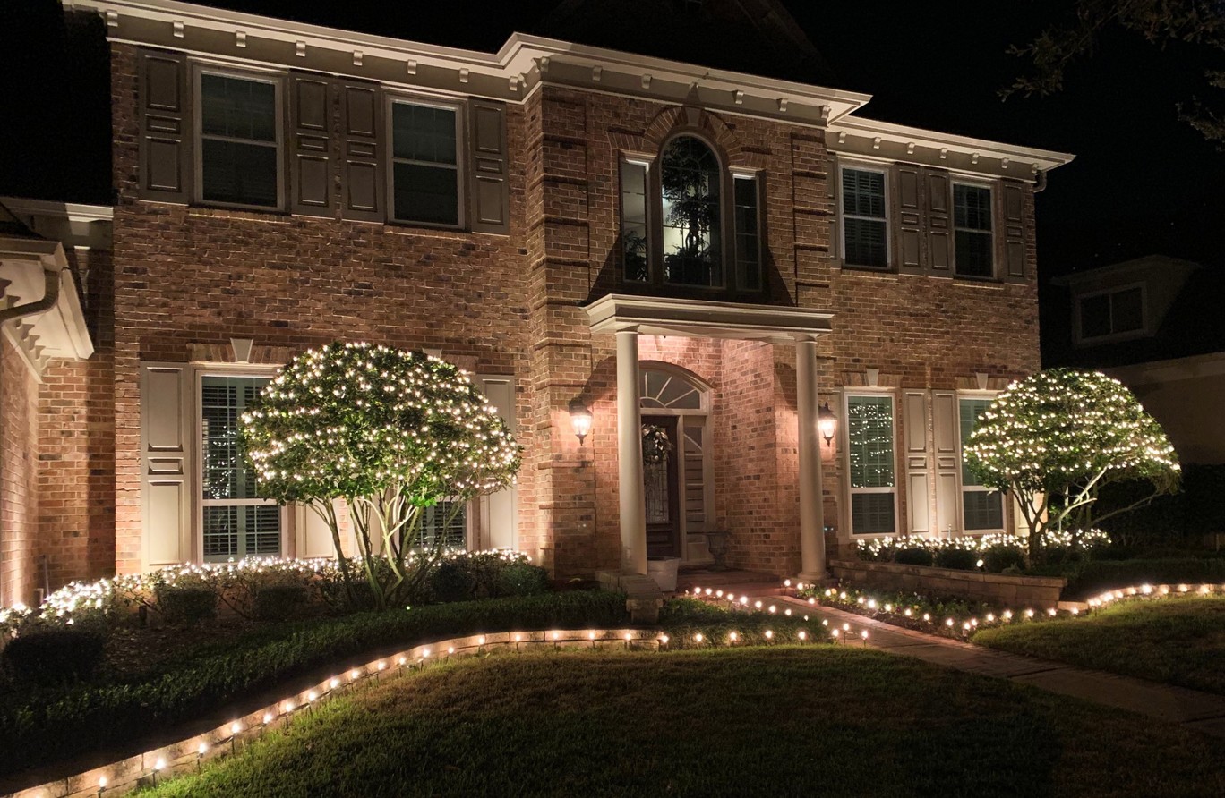 Brick house with winter lights lining the driveway and decorating the trees in front of the house