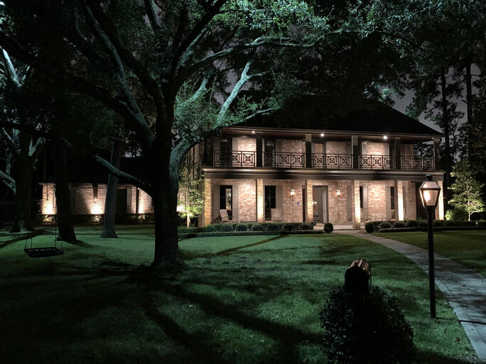 A 2 story brick memorial villages houston home with a balcony and trees in front