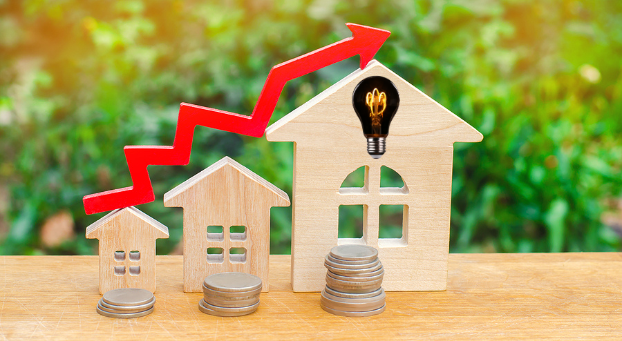 Wooden homes on table with garden in background. Showing red arrow as value increase with stacks of changes increasing with arrow. Home's value.