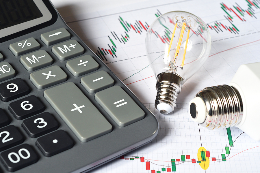 Close up of calculator and energy saving light bulbs over printed graph. Cost benefits.