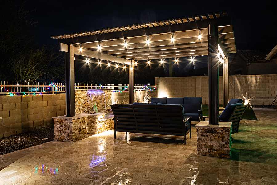 A resort style backyard at night with a waterfall, pergola, and a firepit at night. Patio space.
