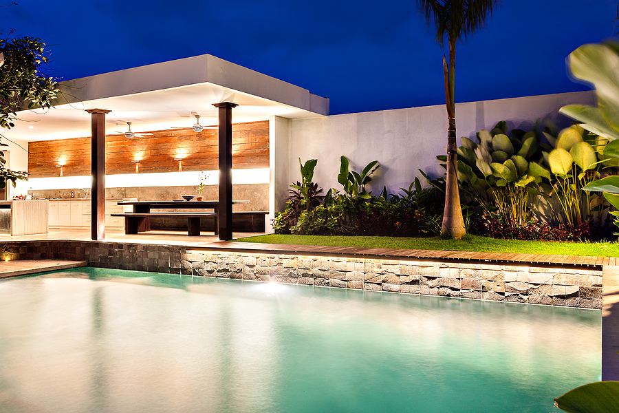 Modern house with a clear swimming pool at night and illuminated using lights in the outdoor dining area beside the garden. curb appeal