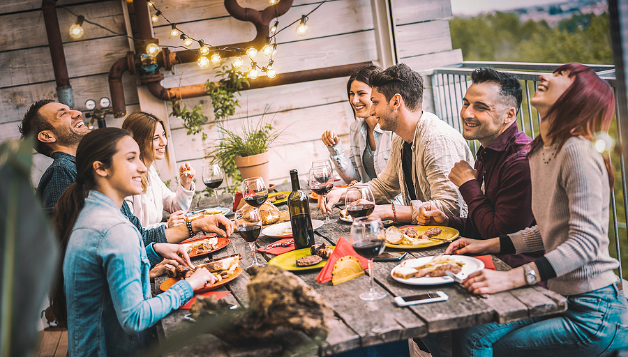 Young people dining and having fun drinking red wine together on balcony rooftop dinner party - Happy friends eating bbq food at restaurant patio - Millannial life style concept on warm evening filter. Barbecue.