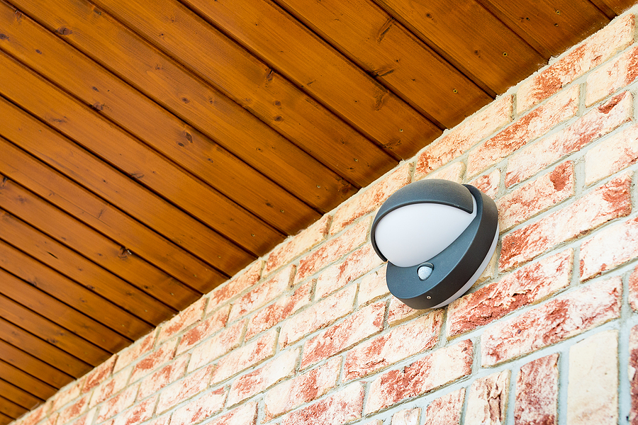 Motion sensor outdoor light mounted on brick wall that is used for motion activated lighting.