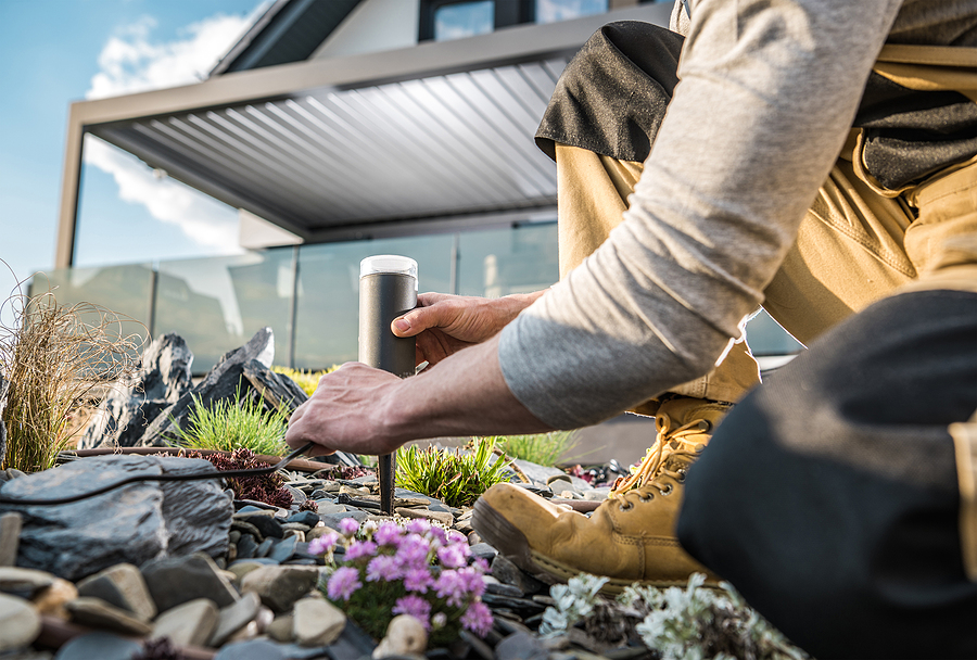 Professional Landscaper kneeling down in a backyard garden installation landscape lights. 