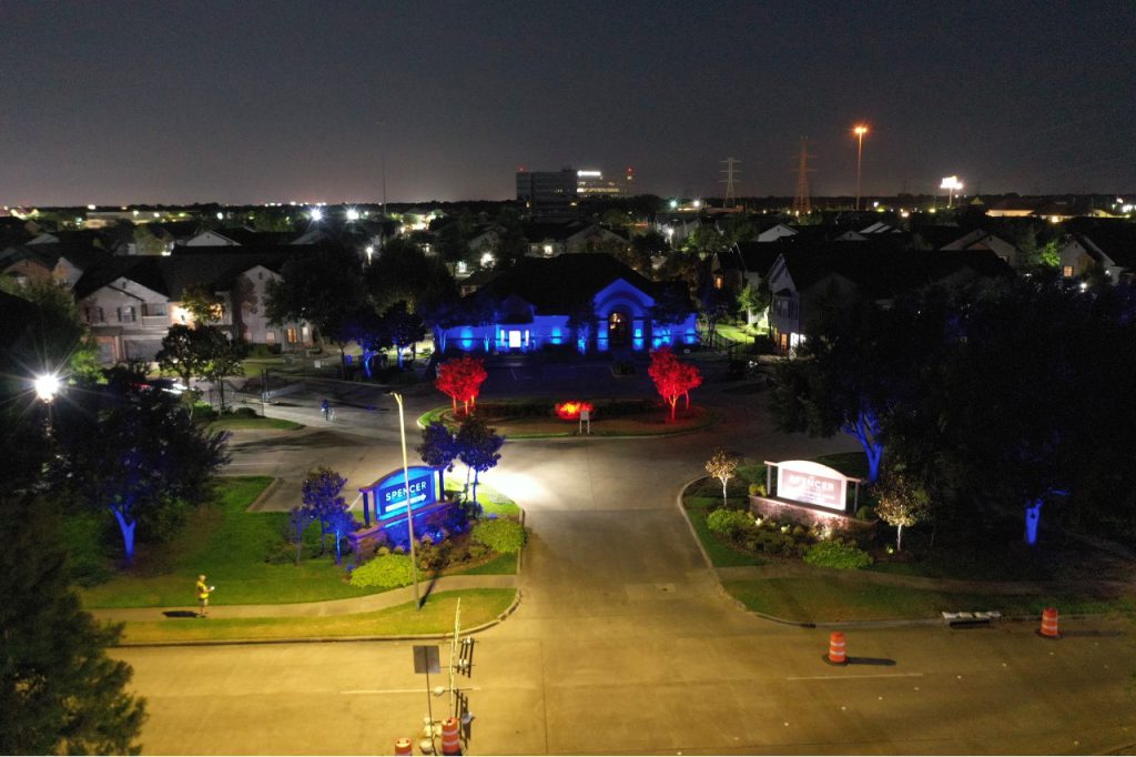 A nighttime photo of an apartment complex entry with landscape lighting illuminating the signage displaying the name of the apartments, highlighting the property’s business identity.
