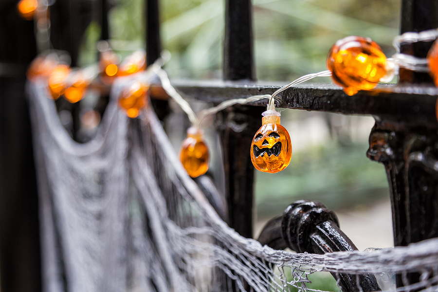Black gate decorated with spiderwebs and glowing jack-o'-lantern lights, creating a festive and spooky Halloween atmosphere.