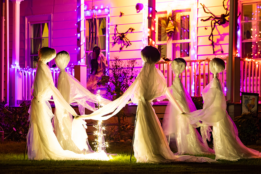Front exterior of a home decorated for Halloween, featuring glowing pumpkins, hanging ghosts, cobwebs, and eerie lighting that casts spooky shadows.