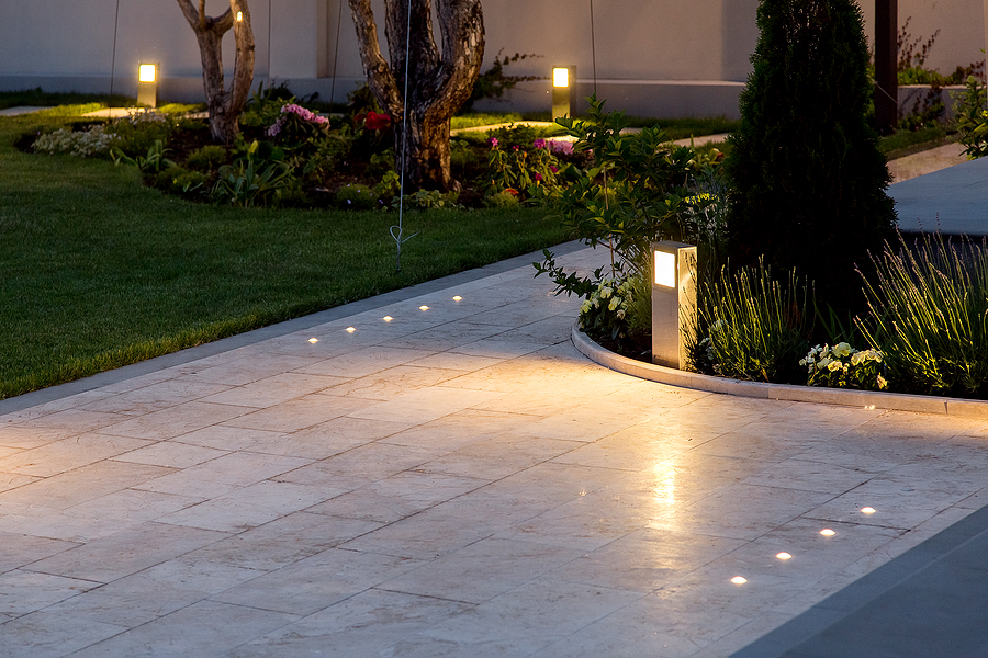Backyard with marble tile patio, flower beds, and lawn, illuminated by ground lanterns and outdoor lighting to enhance security and ambiance.