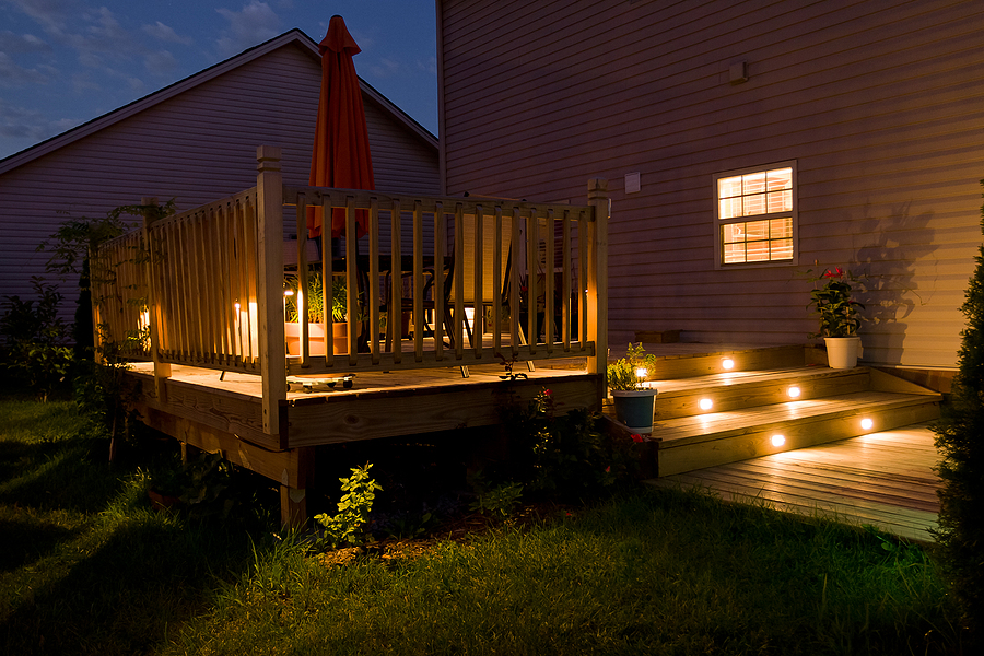 Tranquil backyard with soft outdoor lighting on a wooden deck and patio at night.