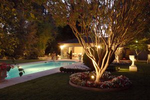 Backyard pool area with warm outdoor lighting showcasing the color contrast between the illuminated patio and the evening sky.