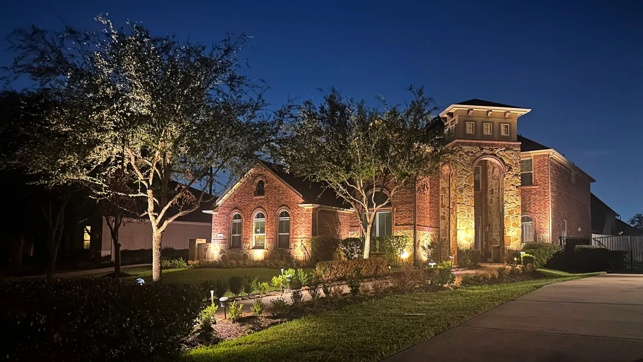 Houston home lit at night, seen from the street across the lawn