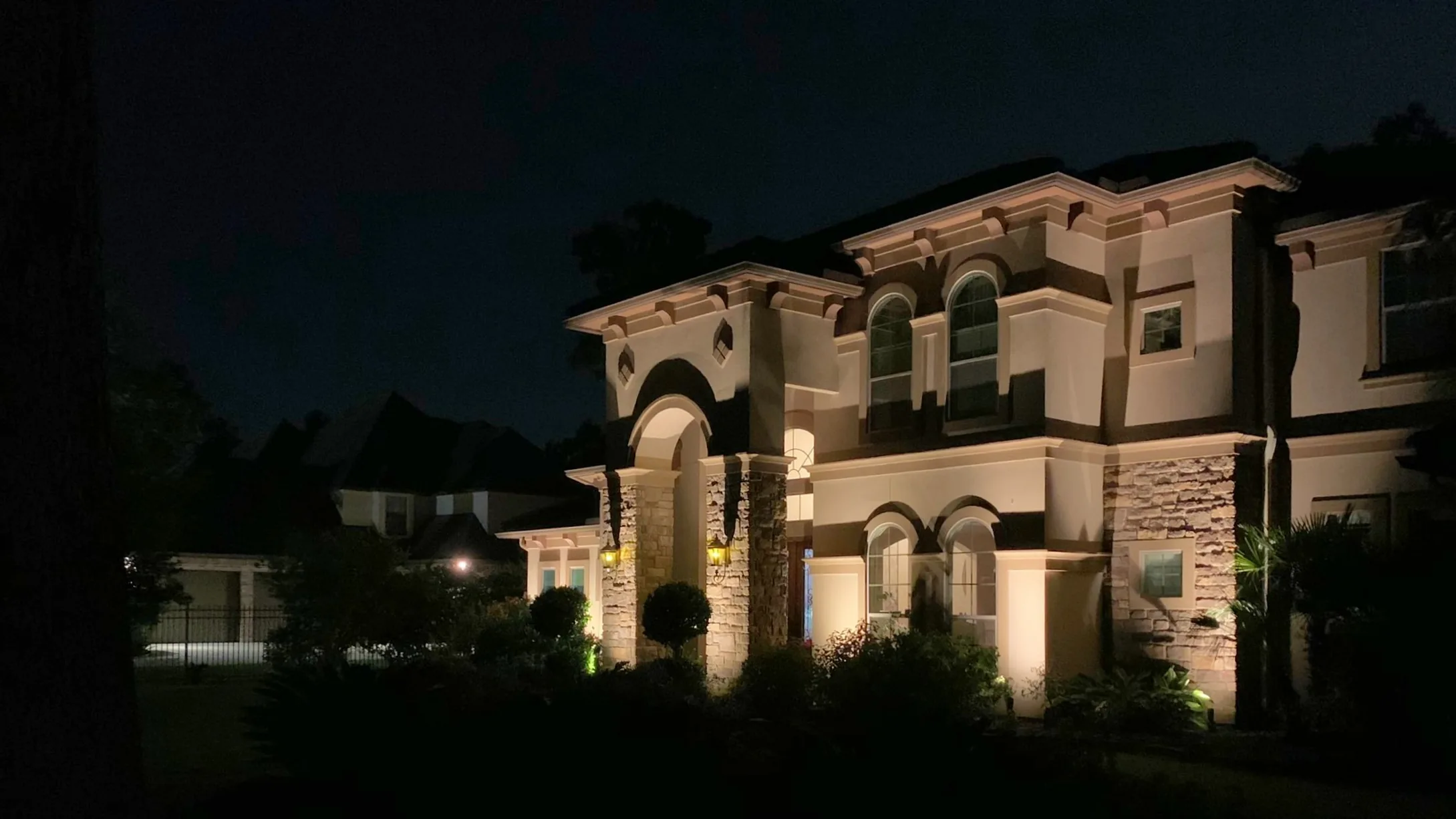 Stone and stucco elevation lit after dark, with the arches and columns picked out