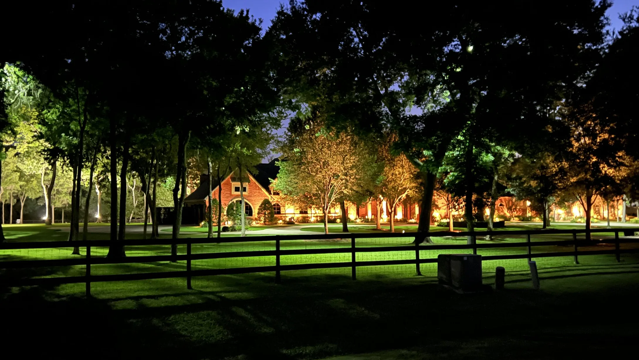 Lawn and mature trees lit at night with a house beyond them