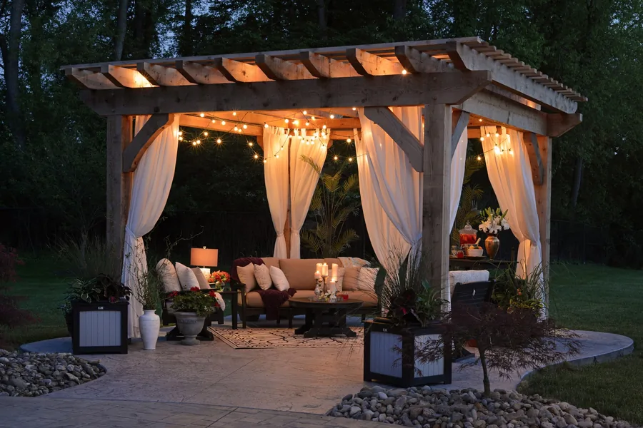 Backyard pergola with seating, string lights and planting lit for the evening