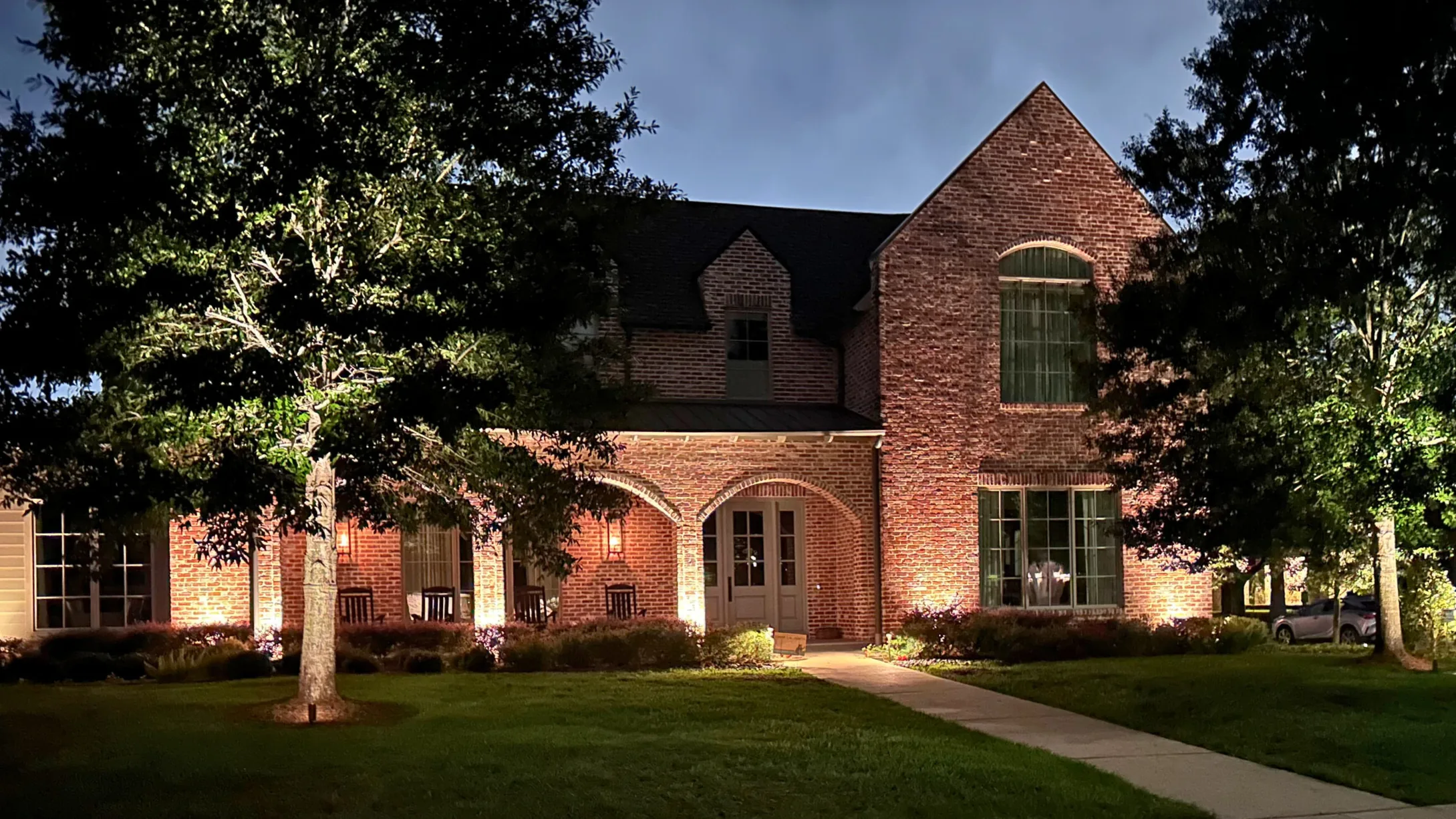 Houston home with the elevation and mature trees lit after dark