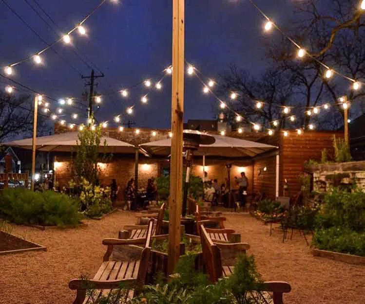 Commercial patio and outdoor seating area lit for evening trade, with planted borders and overhead lighting