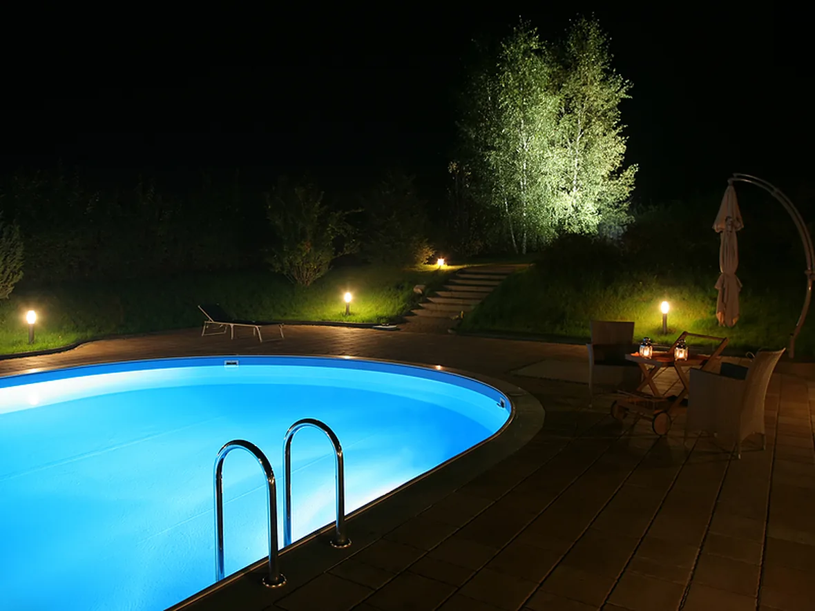 hl-pool-deck-1180.webp Swimming pool at night with the surrounding deck and planting lit and mirrored in the surface