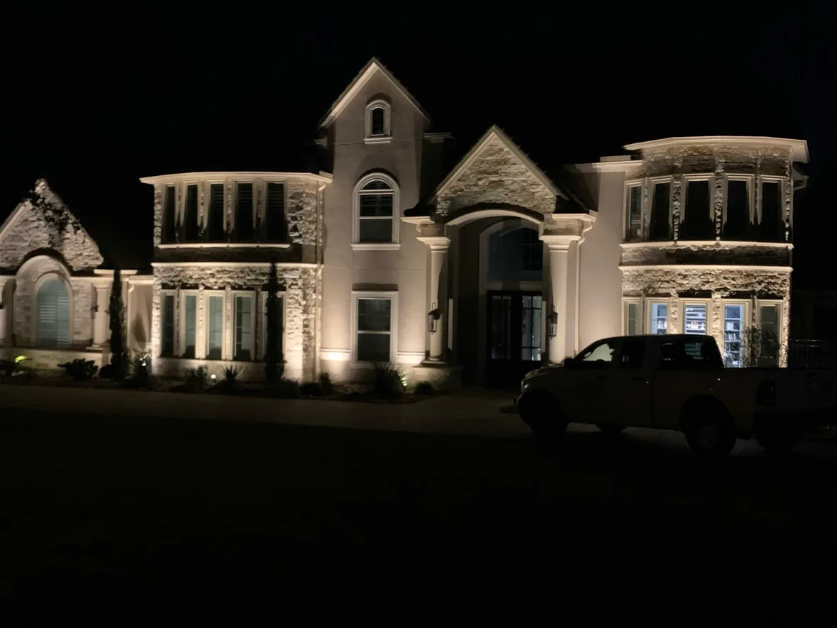 Large house lit at night with the elevation, entry and planting picked out