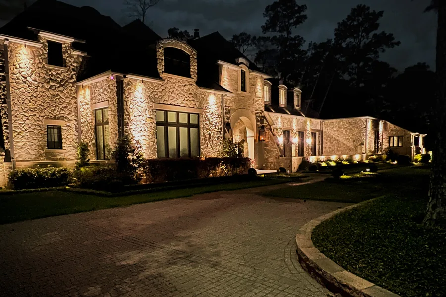 Brick home with a lit entry walkway and uplit trees at the front elevation
