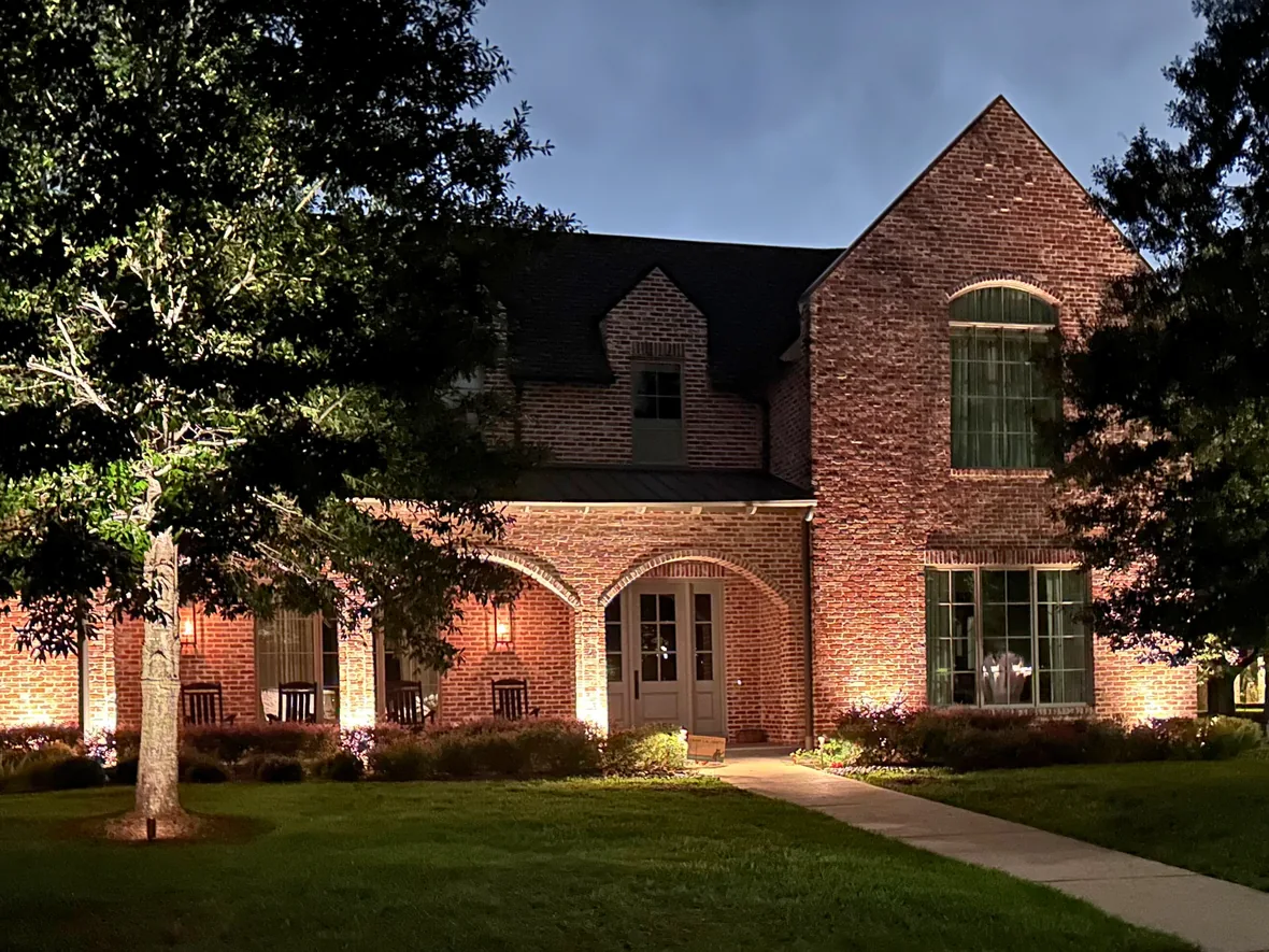 hl-res-front-entry-1180.webp Brick home at dusk with an uplit oak in the front lawn and a lit walkway to the entry